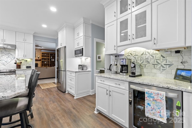 kitchen featuring wine cooler, dark wood-style floors, under cabinet range hood, stainless steel appliances, and white cabinets