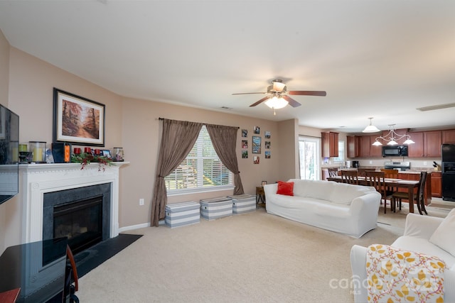 living room featuring a wealth of natural light, a fireplace with flush hearth, light colored carpet, and a ceiling fan