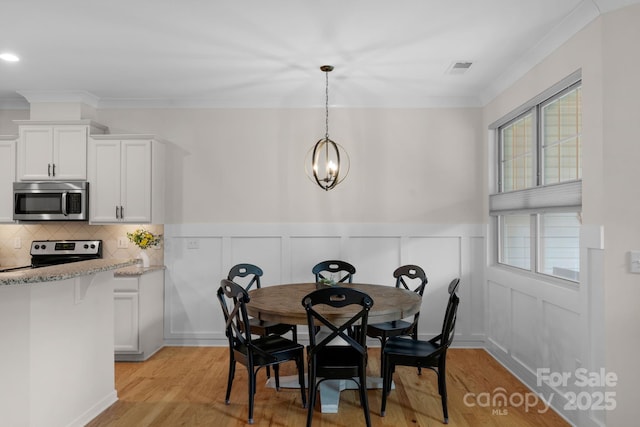 6021 Sweetbay Ln, Indian Land, SC 29707 - dining room featuring a wainscoted wall, crown molding, light wood-style floors, and a notable chandelier