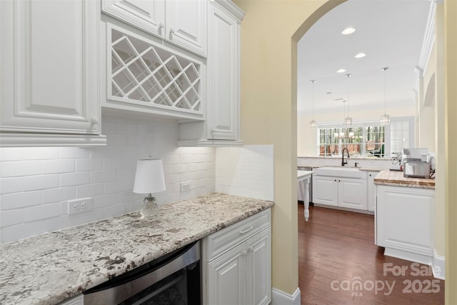 kitchen with beverage cooler, arched walkways, white cabinetry, and a sink
