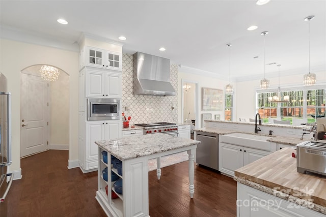 kitchen featuring ornamental molding, a sink, stainless steel appliances, wall chimney range hood, and a chandelier