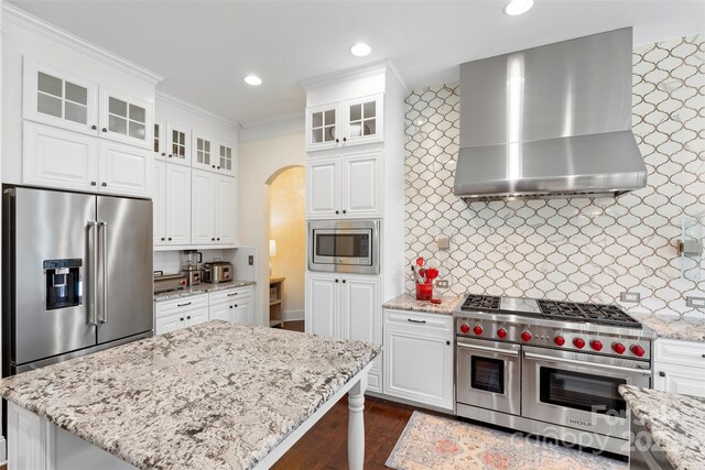 kitchen featuring arched walkways, high quality appliances, wall chimney exhaust hood, and light stone countertops