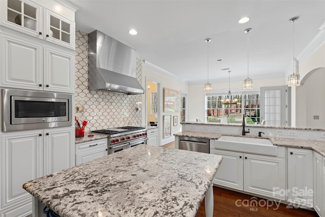 kitchen with crown molding, wall chimney range hood, a chandelier, appliances with stainless steel finishes, and a sink