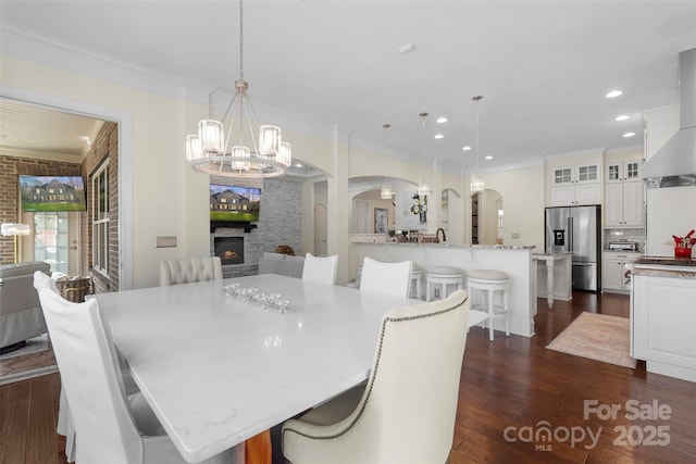 dining area featuring dark wood-style floors, an inviting chandelier, a fireplace, arched walkways, and crown molding
