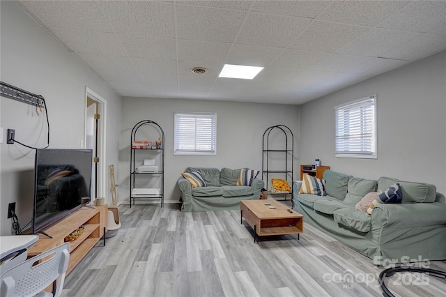 living area featuring light wood-type flooring, a drop ceiling, and a healthy amount of sunlight