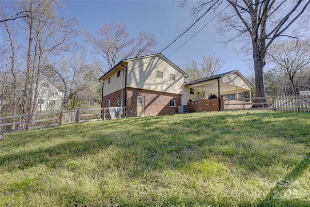 rear view of property with a gate, central air condition unit, a fenced backyard, brick siding, and a yard