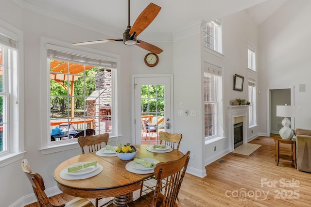 dining room featuring a high end fireplace, a ceiling fan, light wood-style flooring, and a wealth of natural light