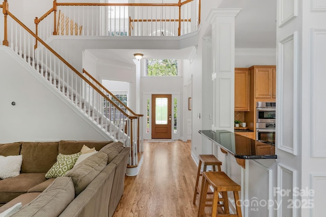interior space featuring stairs, crown molding, light wood finished floors, and a towering ceiling