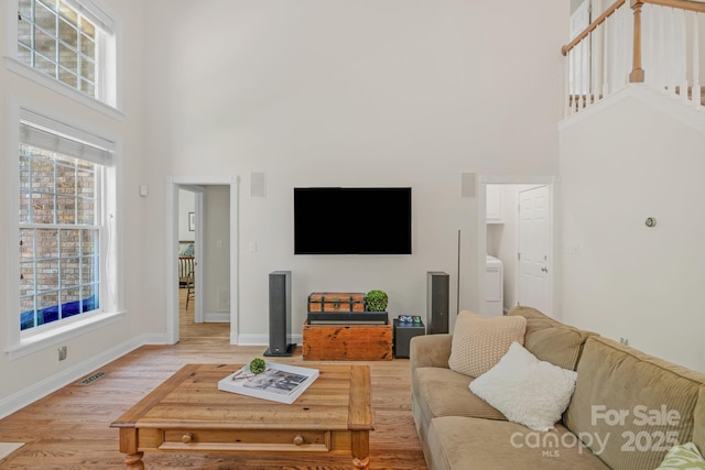 living area featuring a high ceiling, plenty of natural light, baseboards, and light wood-style floors