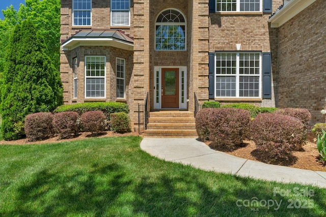 view of exterior entry with brick siding and a lawn