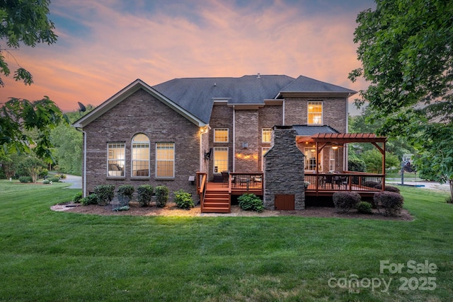 back of property at dusk featuring a wooden deck, a pergola, a yard, and brick siding