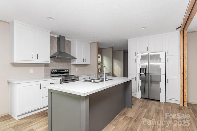 kitchen with wall chimney exhaust hood, a sink, appliances with stainless steel finishes, white cabinets, and light wood finished floors
