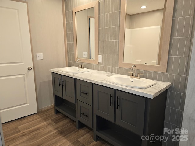 bathroom with double vanity, wood finished floors, tasteful backsplash, tile walls, and baseboards