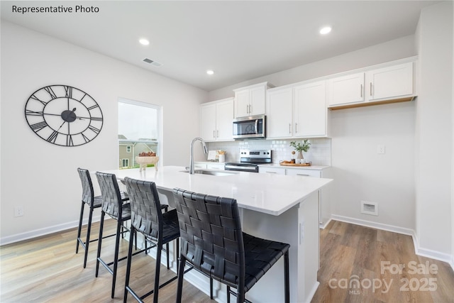 kitchen featuring white cabinets, stainless steel appliances, visible vents, a sink, and decorative backsplash