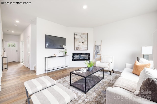 living area featuring baseboards, a glass covered fireplace, light wood finished floors, and recessed lighting