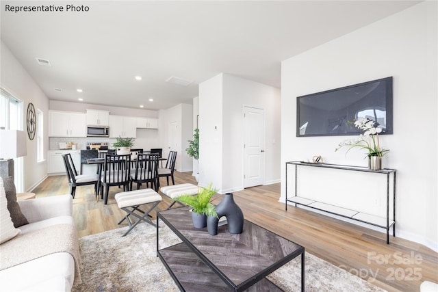 living room featuring recessed lighting, baseboards, visible vents, and light wood-type flooring