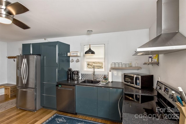 kitchen featuring a sink, wall chimney range hood, appliances with stainless steel finishes, dark countertops, and light wood-style floors