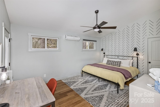 bedroom with baseboards, a wall mounted air conditioner, an accent wall, ceiling fan, and wood finished floors