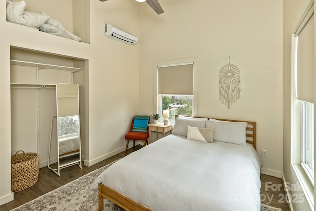 bedroom featuring baseboards, a wall mounted air conditioner, ceiling fan, dark wood finished floors, and a towering ceiling