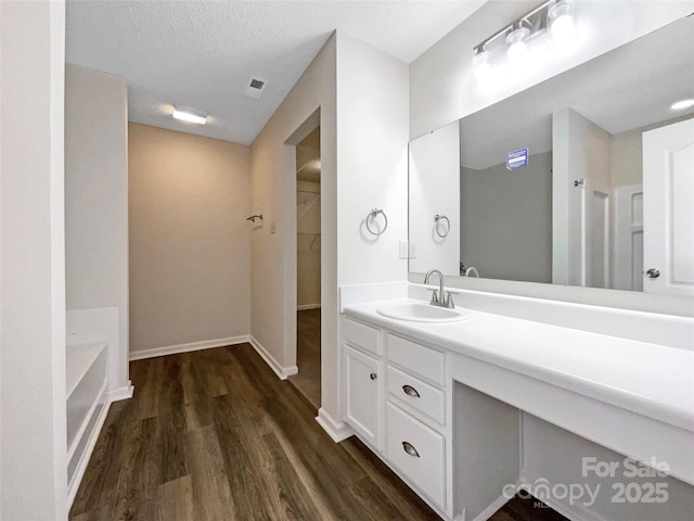 full bathroom with a textured ceiling, wood finished floors, vanity, baseboards, and a spacious closet