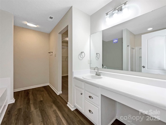 bathroom with vanity, wood finished floors, visible vents, baseboards, and a walk in closet