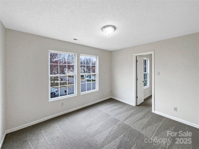 carpeted spare room featuring visible vents, baseboards, and a textured ceiling