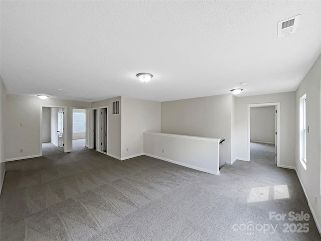 empty room with carpet flooring, baseboards, visible vents, and a textured ceiling