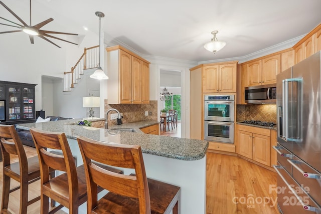 kitchen with light stone counters, a peninsula, a breakfast bar area, appliances with stainless steel finishes, and a sink