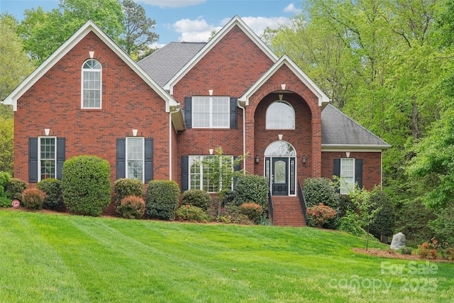 view of front facade with roof with shingles, brick siding, and a front lawn