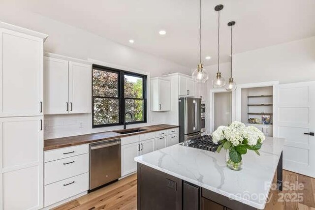 kitchen featuring a kitchen island, light wood-type flooring, white cabinets, a sink, and stainless steel appliances