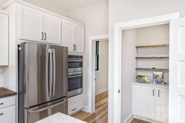 kitchen with open shelves, light wood-type flooring, baseboards, stainless steel appliances, and white cabinetry