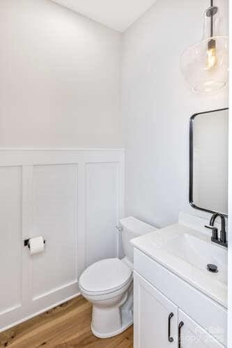 bathroom with a decorative wall, toilet, wood finished floors, and vanity