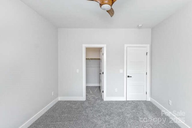 unfurnished bedroom with a walk in closet, ceiling fan, baseboards, a closet, and carpet flooring