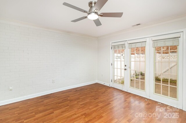 unfurnished room with brick wall, a ceiling fan, baseboards, ornamental molding, and wood finished floors