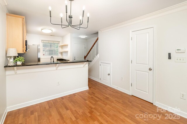 kitchen with an inviting chandelier, open shelves, light wood-type flooring, a peninsula, and freestanding refrigerator