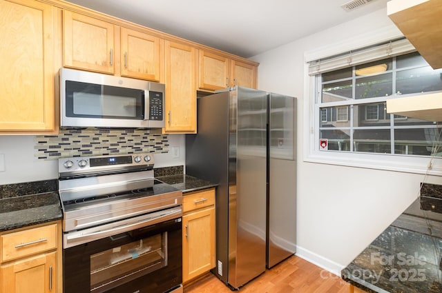 kitchen with appliances with stainless steel finishes, light wood-style floors, light brown cabinetry, and dark stone countertops