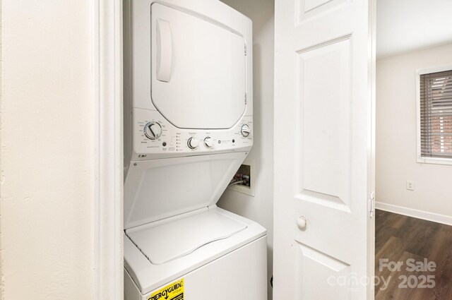 clothes washing area featuring stacked washer / drying machine, dark wood-style floors, laundry area, and baseboards