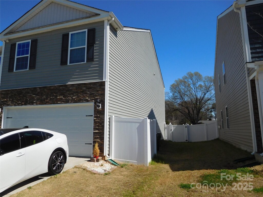 view of home's exterior with a gate, fence, driveway, a garage, and stone siding