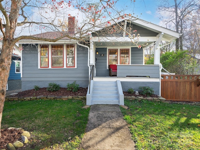 bungalow-style house with a front lawn, fence, covered porch, and a chimney