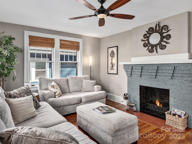 living room with baseboards, a brick fireplace, wood finished floors, and a ceiling fan