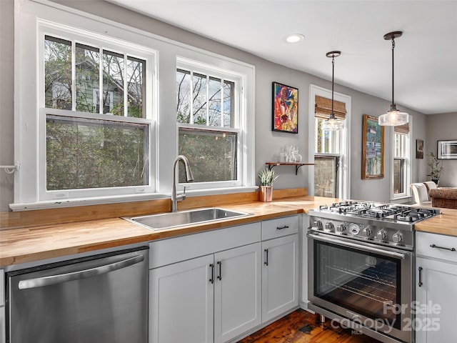 kitchen with dark wood-style flooring, a sink, stainless steel appliances, pendant lighting, and butcher block counters