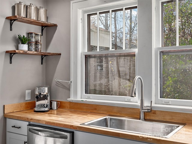 kitchen featuring a sink, stainless steel dishwasher, white cabinetry, wood counters, and open shelves