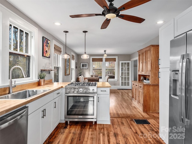 kitchen featuring wood finished floors, a peninsula, a sink, butcher block countertops, and stainless steel appliances