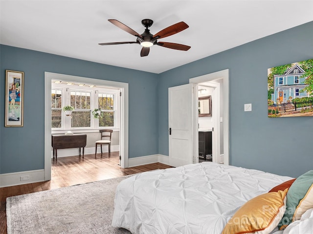 bedroom with a ceiling fan, wood finished floors, baseboards, and ensuite bathroom