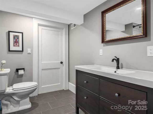 bathroom with visible vents, toilet, vanity, baseboards, and wood tiled floor