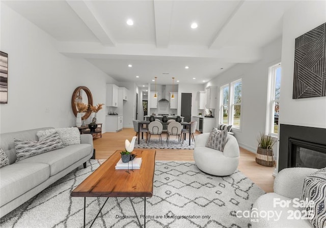living area with light wood-style flooring, beam ceiling, recessed lighting, and a glass covered fireplace