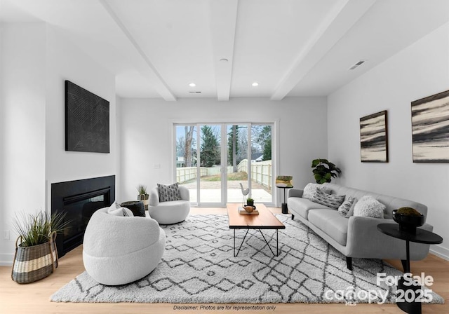 living room featuring beamed ceiling, wood finished floors, a glass covered fireplace, baseboards, and recessed lighting