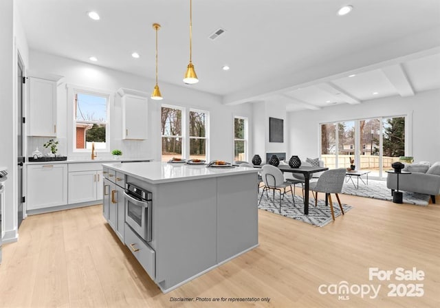 kitchen featuring open floor plan, light wood finished floors, oven, beam ceiling, and white cabinets