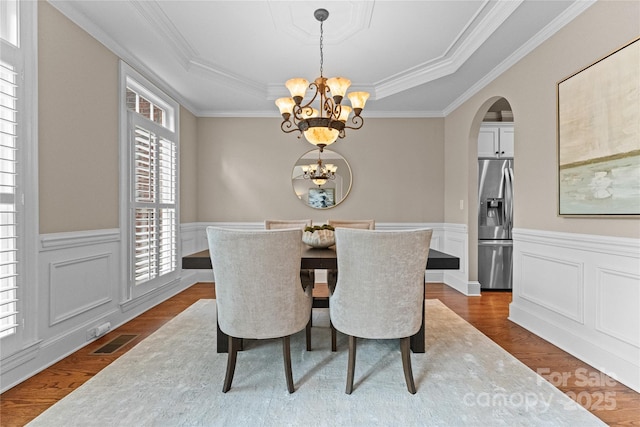 dining area with arched walkways, an inviting chandelier, dark wood-style flooring, and a raised ceiling