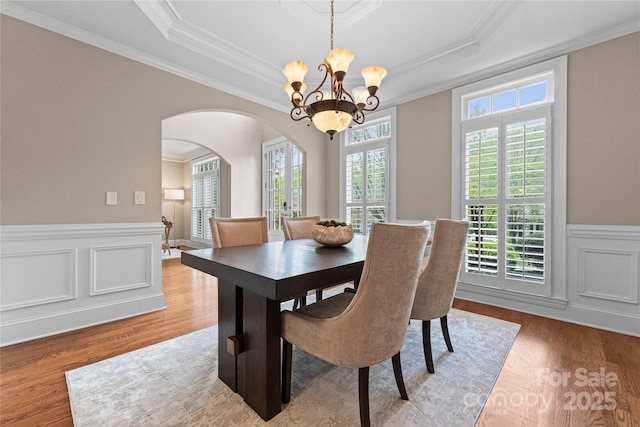 dining space with arched walkways, a notable chandelier, ornamental molding, and wainscoting